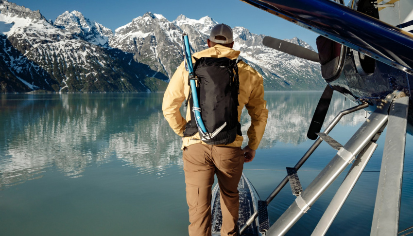 男人背著背包，站在阿拉斯加湖上的水上飛機上