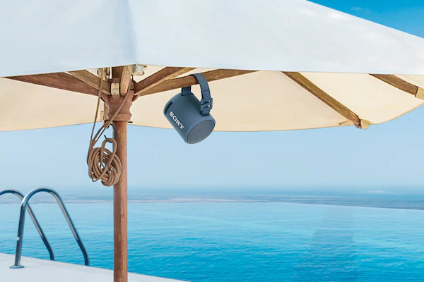 XB13 EXTRA BASS(TM) 便攜式無線揚聲器連接到熱帶海灘上的遮陽傘的圖片。