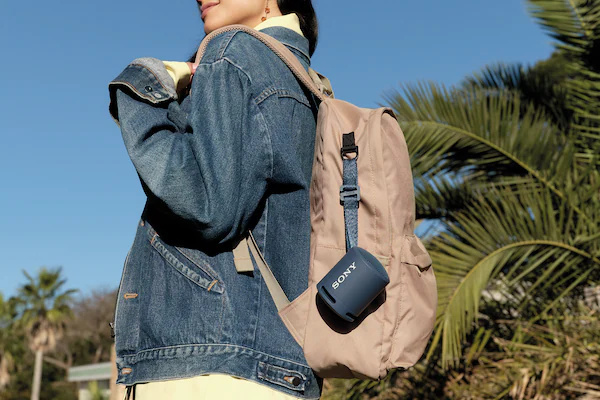 XB13 EXTRA BASS(TM) 便攜式無線揚聲器安裝在一位年輕女性的背包上的圖片。